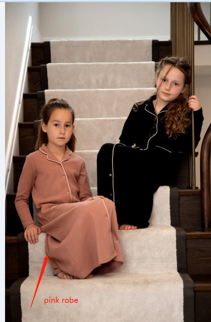 Two girls wearing FashionRay robes, one in pink and one in black, sitting on a staircase.