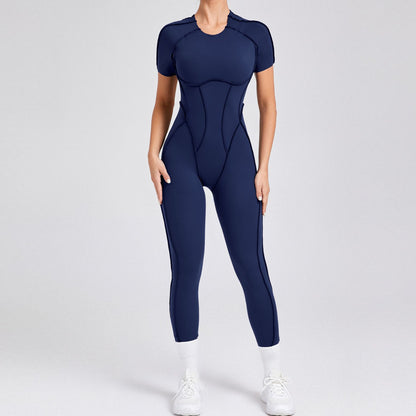 Woman modeling navy blue fitted jumpsuit with short sleeves, white sneakers, and socks on plain background