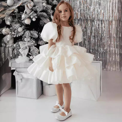 Girl in a white ruffled dress by silver Christmas tree, FashionRay festive kids fashion.