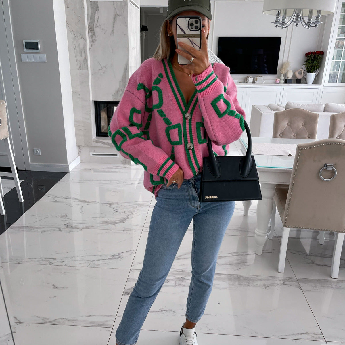 Woman in pink green geometric cardigan, blue jeans, black handbag in modern living room