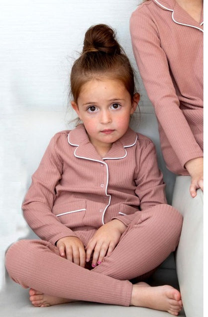 Young girl in mauve ribbed pajamas with white trim sitting on sofa, FashionRay loungewear style