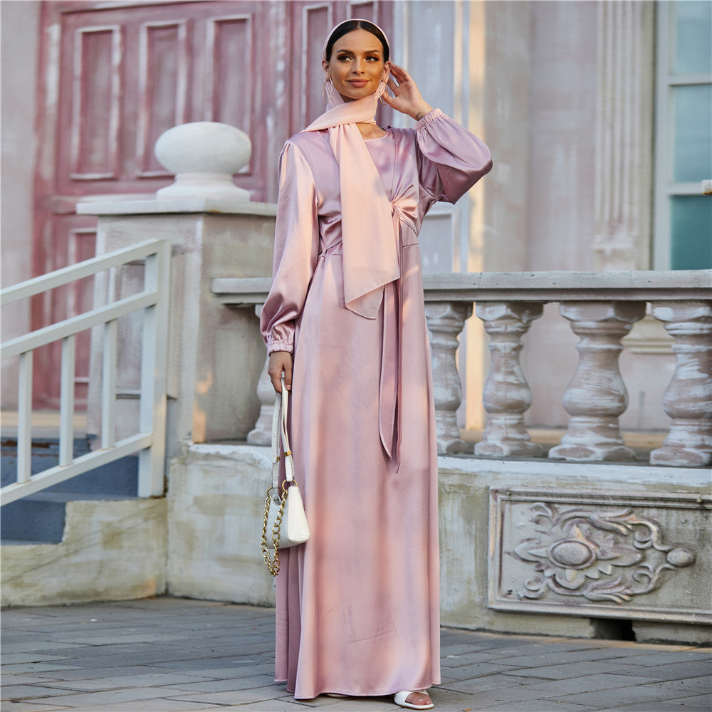 Woman in elegant satin pink maxi dress with scarf, holding white handbag, outdoor fashion look