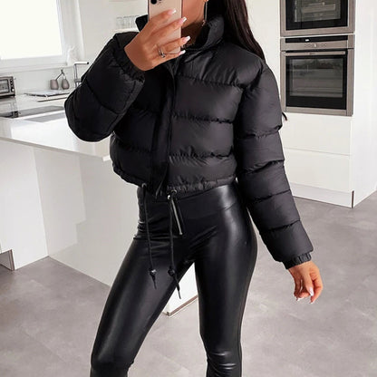 Woman in trendy black puffer jacket and faux leather leggings posing in modern kitchen