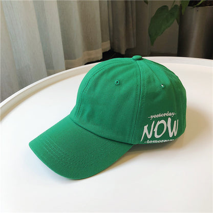 Green FashionRay baseball cap with bold NOW text, displayed on a white table indoors